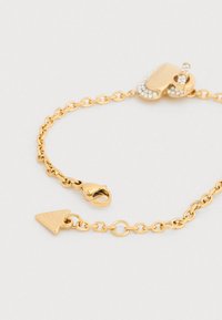 Βραχιόλι αλυσίδας από χρυσό με στρογγυλούς κρίκους, τριγωνική ετικέτα και κούμπωμα διακοσμημένο με καθαρά στρας. Λείο μεταλλικό φινίρισμα.