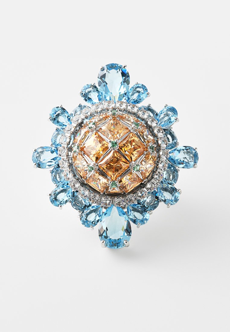 Broche en bijouterie avec une pierre précieuse orange centrale entourée de pierres claires et bleu clair, dans un design rond et complexe.