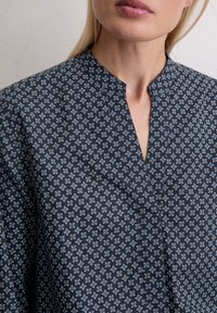 Marineblauwe blouse met patroon en een mandarin nek, voorzien van een geometrisch ontwerp in lichtblauw en wit. Zachte, gestructureerde stof.