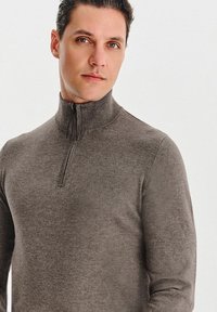 Brązowy sweter z zamkiem na szyi o dopasowanym kroju. Wykonany z miękkiej dzianiny, z teksturowanym wykończeniem i wysokim kołnierzem.