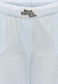 Pantalons bleu clair en tissu doux avec une taille élastique. Présente une poche latérale et une étiquette avec "Next Generation".