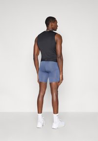 Μαύρο αμάνικο τοπ και εφαρμοστά μπλε σορτς, κατασκευασμένα από ελαστικό ύφασμα. Διακοσμημένη ζώνη μέσης με λογότυπο, συνδυασμένα με λευκά αθλητικά παπούτσια και κάλτσες.