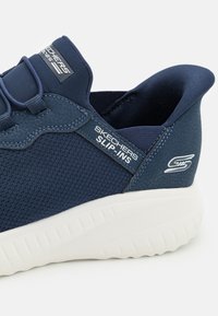 Slip-Ins Skechers blu navy con parte superiore in tessuto testurizzato, lacci elastici e suola in gomma bianca. Presenta il logo del marchio sul lato.