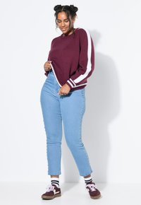 Vinröd stickad tröja med vita ränder på ärmarna, i kombination med ljusblå jeans som har nitar längs sidorna.