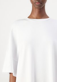 Bijela oversized majica od mekog pamuka s okruglim izrezom i širokim, kratkim rukavima. Glatka tekstura, minimalistički dizajn, bez uzoraka.