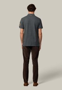 Uhlový polo tričko s golierom, krátkymi rukávmi a vyšitým dizajnom na ľavom rukáve. Skombinované s hnedými nohavicami a hnedými topánkami.