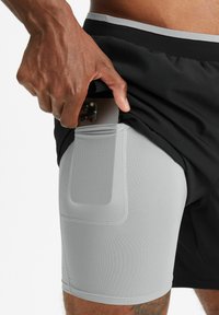 Schwarze Sportshorts mit einer hellgrauen, strukturierten Innenhose und einer Tasche, die dafür ausgelegt ist, ein Smartphone sicher zu halten.