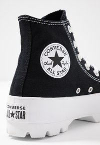 Czarne trampki typu high-top z białą gumową podeszwą, z okrągłym logo z gwiazdą i tekstem oraz białymi przeszyciami.