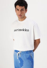 Balta kokvilnas T-krekls ar melnu uzrakstu "marimekko". Apvienots ar zilām svītrainām sporta biksēm ar auklu jostu.