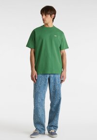 T-shirt verde in cotone a maniche corte con un logo sul petto, abbinato a pantaloni di denim blu con un motivo a fiamma e una vestibilità rilassata.