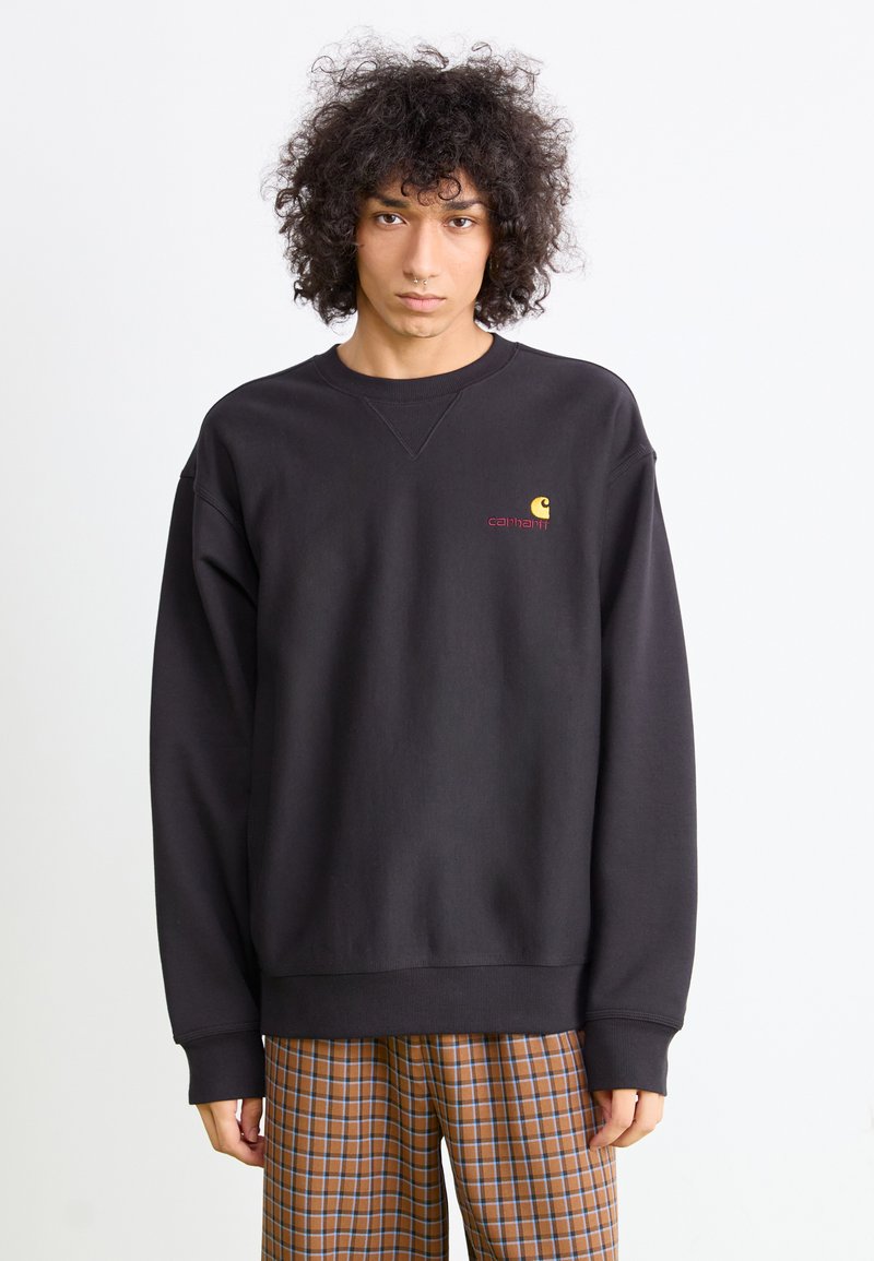 Zwarte sweatshirt met geribbelde manchetten en zoom, met een klein geel en rood logo op de borst. Zacht, gestructureerd materiaal; ontspannen pasvorm.