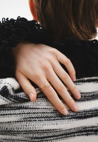 Anillo cruzado de oro en un dedo delgado, descansando sobre una tela de punto a rayas blancas y negras con una textura suave.