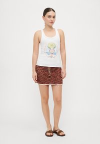 Top blanco sin mangas con estampado gráfico; falda marrón con patrón y dobladillo en forma de escallona; sandalias marrones; textura suave y diseño ajustado.