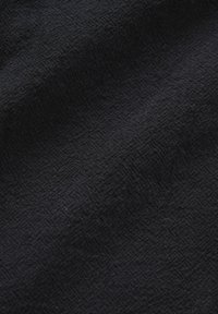 Black textured fabric with a subtle grid pattern and soft folds creating light and shadow variations across the surface.