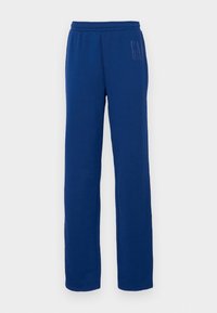 Mörkblå träningsoverallsbyxor i mjuk tyg, med resår i midjan och en subtil logotypdesign på vänster sida. Rak benmodell.