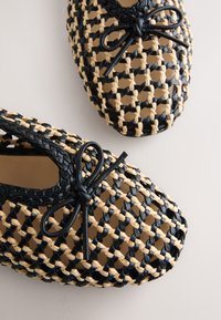 Ballerines tissées noir et beige avec petits nœuds sur les orteils, montrant un motif en maille ouverte détaillé et une doublure intérieure lisse.