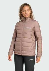 Brązowa izolowana kurtka z wysokim kołnierzem i zapięciem na zamek, z poziomym przeszyciem i wyszywanym logo TERREX na piersi.