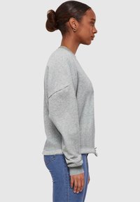 Grijze sweater met lange mouwen, geribbelde boorden en een relaxte pasvorm. Heeft een subtiele textuur en een trekkoord aan de zoom voor aanpasbaarheid.