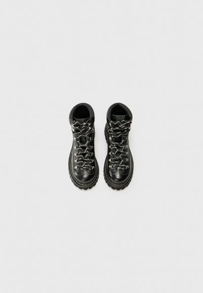 Botas de senderismo de cuero negro con cordones plateados y negros, un collar acolchado y suelas de goma gruesas con patrones de pisada distintivos.