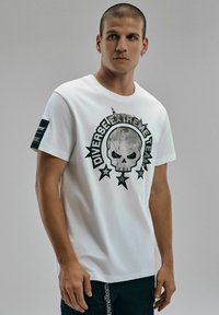 Biała koszulka z bawełny z czarną grafiką czaszki z gwiazdami i napisem "Diverse Extreme Team", wyposażona w czarną metkę na rękawie.