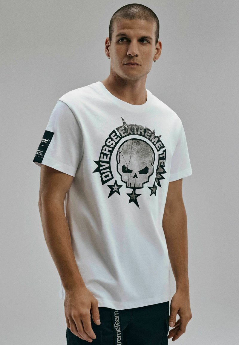 Biała koszulka z bawełny z czarną grafiką czaszki z gwiazdami i napisem "Diverse Extreme Team", wyposażona w czarną metkę na rękawie.