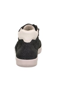 Černá texturovaná teniska s bílou podrážkou a nákolenicí, viděná zespodu, na bílém pozadí.