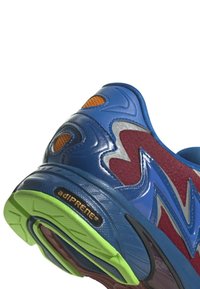 Modrá atletická bota s texturovaným svrškem, červenými akcenty a zelenou gumovou podrážkou. Má vzdušné síťované části a logo adiPRENE.