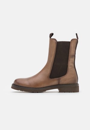 Bota Chelsea de cuero marrón con paneles laterales elásticos oscuros, tiradores, tacón bajo y suela con dibujo sobre un fondo liso.