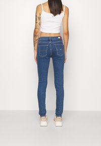 Vaqueros skinny de color azul con una textura de denim suave, con bolsillos traseros y un parche con logotipo en la cinturilla. Combinados con zapatillas de colores claros.