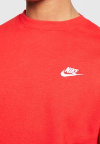 Nike-tröja i klart röd bomull, med rund hals och en liten vit logga på bröstet, med en slät yta.