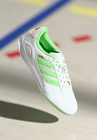 Scarpa sportiva bianca con accenti verdi, texture in rete e design a tre strisce. Presenta una punta arrotondata e un interno imbottito.