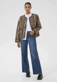 Veste surdimensionnée à imprimé léopard avec bordure noire, portée sur une chemise blanche. Associée à un jean en denim taille haute et à jambes larges, ainsi qu'à des chaussures noires.