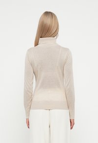 Pull en beige à col roulé avec des manches longues, des poignets côtelés et un ourlet. Tissu doux avec une texture lisse, légèrement plus claire près du bas.