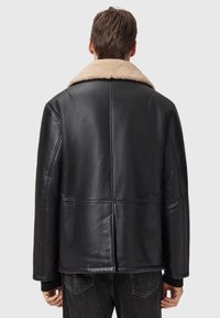 Sort læderjakke med en beige fåreskindsjakke, der har en afslappet pasform, synlige sømme og en glat tekstur.