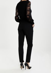 Haut noir avec des manches longues en dentelle, associé à un pantalon noir slim et des chaussures à talons hauts noires. Texture douce et design ajusté.