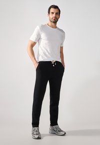 Schwarze Jogginghosen mit Kordelzugbund und Seitentaschen, kombiniert mit einem weißen Rundhals-T-Shirt und grauen Sportschuhen. Einfaches Design.