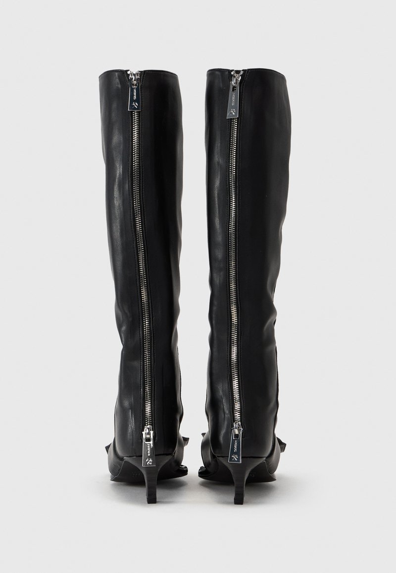 Knelånga svarta läderstövlar med en slät yta, utrustade med silverfärgade sidodragkedjor och en liten klack. Inga synliga mönster eller ytterligare detaljer.