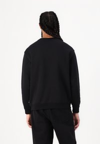 Czarny sweatshirt z długimi rękawami, ściągaczami przy mankietach i u dołu. Gładka tekstura, prosty design i standardowy krój, noszony z czarnymi spodniami.