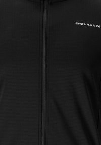 Veste zippée noire en tissu texturé. Présente une fermeture éclair frontale et un logo sur la zone de la poitrine. Design simple sans motifs ni accents.