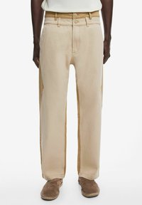 Beige wide-leg pants made of soft cotton with dual button closure, featuring side pockets and contrasting stitching detail.