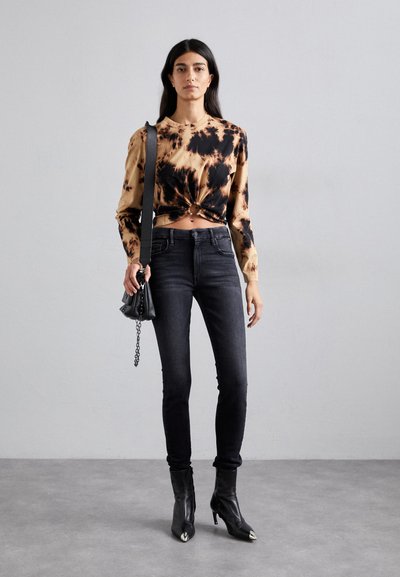 Langermet tie-dye topp i beige og svart, kombinert med høytekkede svarte skinny jeans og spisse ankelstøvler. Liten svart håndveske inkludert.