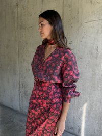 Červené a černé šaty s květinovým vzorem, s hlubokým výstřihem, dlouhými rukávy a vázaným šátkem na krku. Hladká textura.