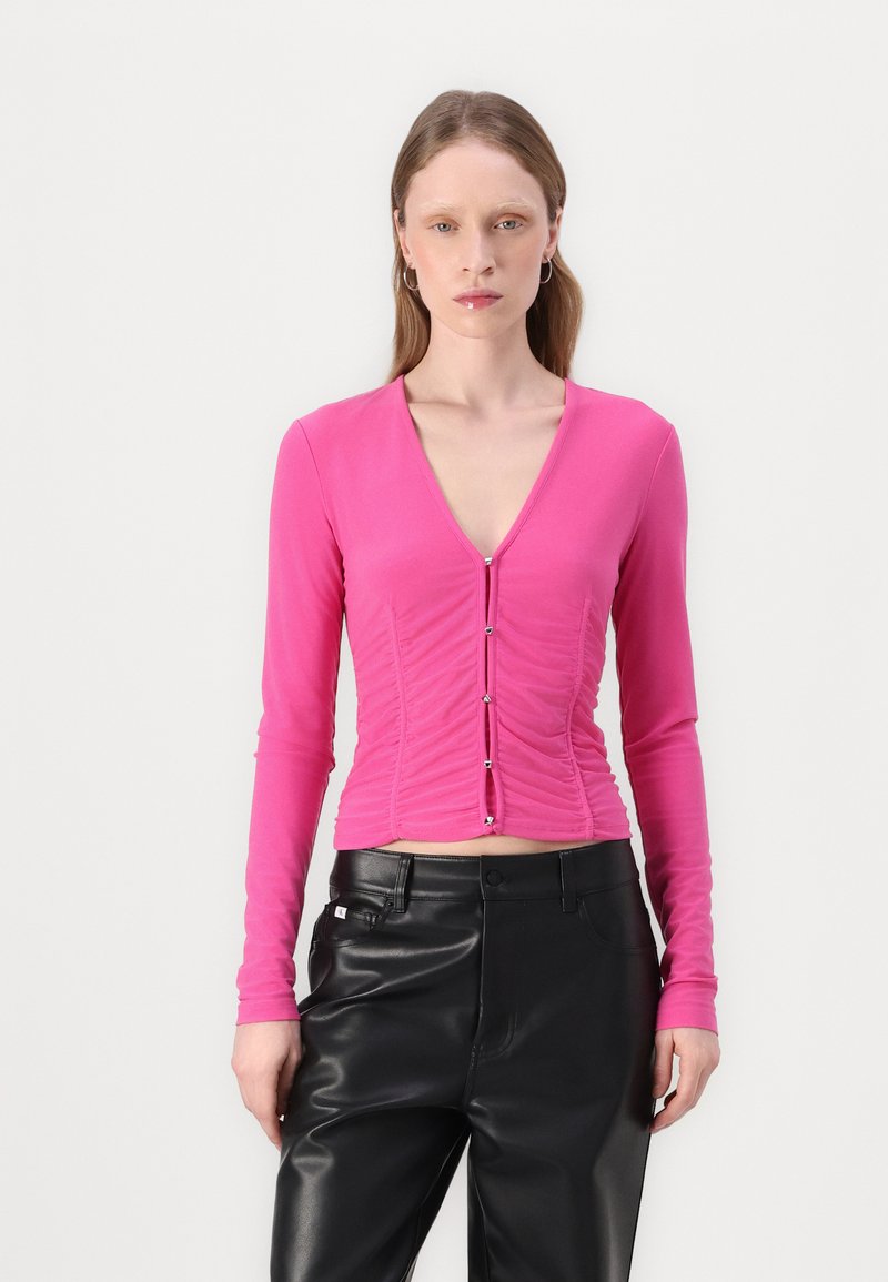 Fitted, long-sleeve pink top with a deep V-neck, ruched texture, and silver button details down the front, paired with black leather pants.