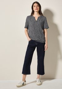 Blusa a maniche corte bianca e nera a fantasia con scollatura a V, abbinata a jeans cropped blu scuro e sneakers bianche con dettagli neri.