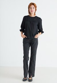 Black shirt with subtle dot pattern, loose fit, gathered sleeve details. Black high-waisted pants with side slits at the hem. Black flats with studs.