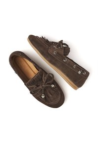 Braune Wildleder-Mokassins im Stil mit Fransenverzierungen, Schnürverschluss und silbernen Hardware-Elementen auf einer flexiblen beige Sohle.