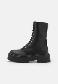 Botte de combat en cuir noir avec un laçage sur le devant, des œillets métalliques, et une semelle épaisse noire avec une texture nervurée.