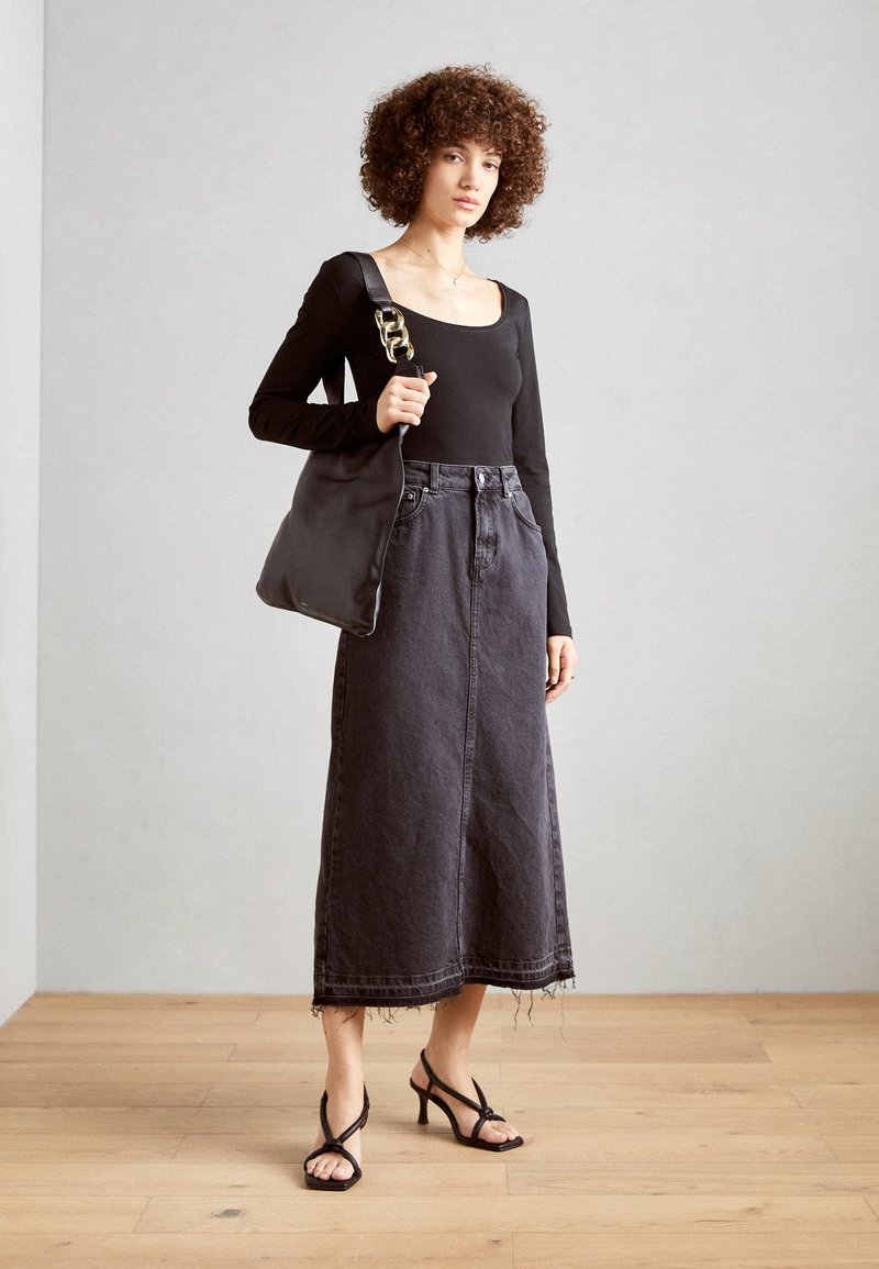 Blusa negra de manga larga, falda midi de mezclilla negra de cintura alta con dobladillo deshilachado y sandalias de tacón negro con tiras. Bolso negro con detalles dorados.