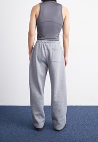 Szare dresy o luźnym kroju, z elastycznym pasem i tylną kieszenią. Tkanina wydaje się miękka i gładka w dotyku. Widok od tyłu.