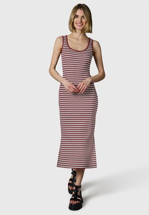 Kobieta uśmiechająca się, ubrana w sukienkę midi bez rękawów w bordowo-białe paski oraz czarne sandały na platformie, stojąca na tle jasnoszarym.